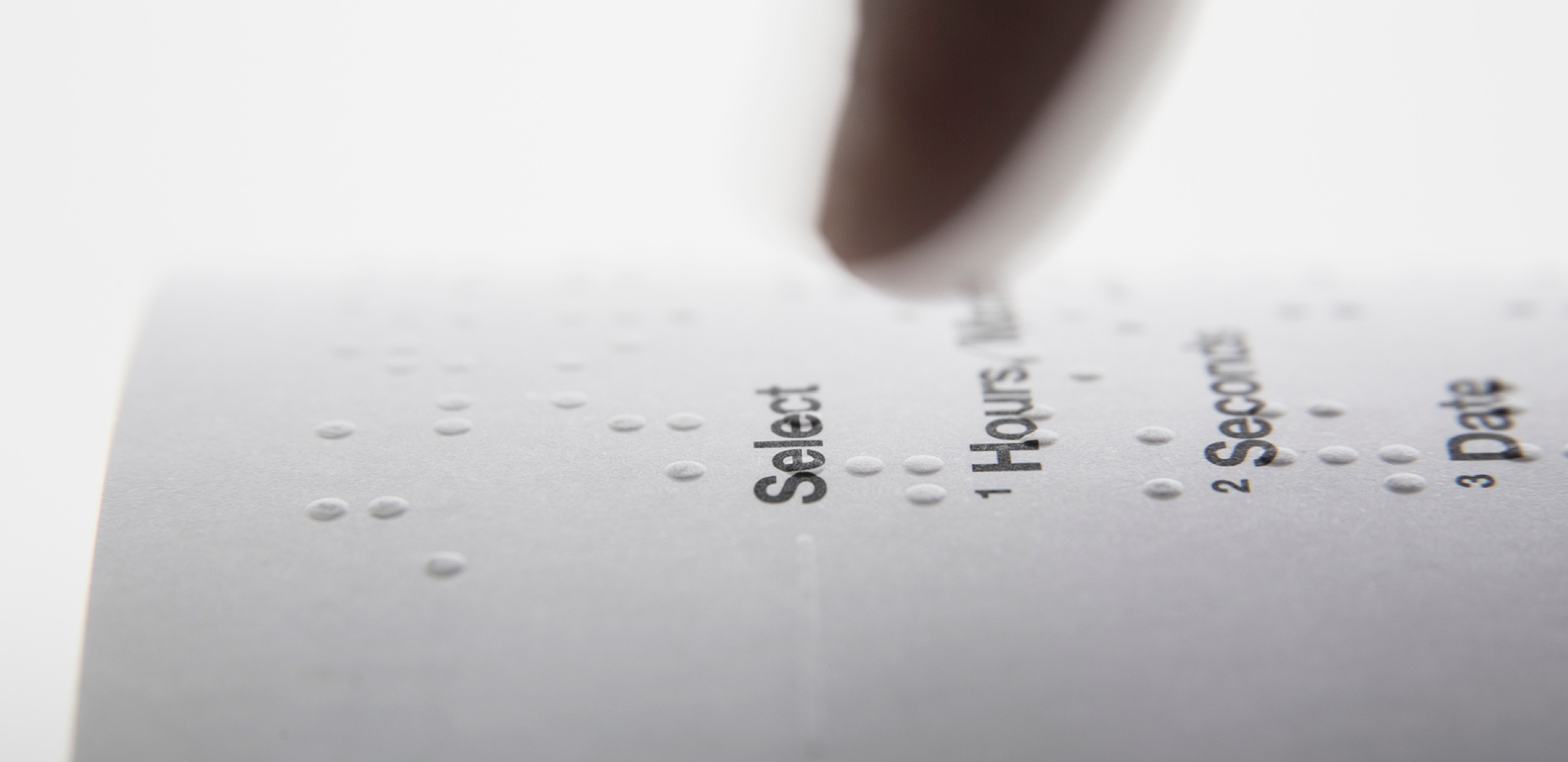 A finger touching the Braille dots of Dot Watch Manual